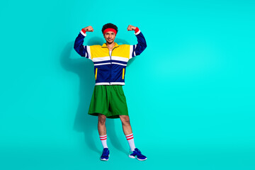 Young athletic man in retro activewear posing confidently against vibrant teal background, embracing fitness and vintage style