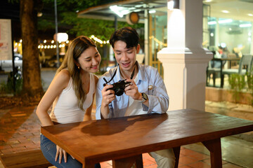 Two friends enjoy reviewing photos on a camera after a fun evening. Capturing memories together at a cozy outdoor spot during their night out