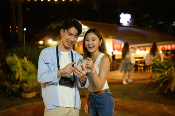 Two cheerful friends enjoy reviewing photos on a smartphone together during a lively night market visit