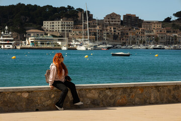 Red haired woman wearing glasses sitting on the seafront watching the scenery on a sunny day with the blue sea in the background