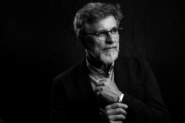 Black and white portrait of a handsome mature man with confident expression. Chiaroscuro lighting on dark background adds dramatic, timeless, and elegant mood.