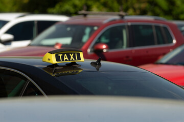 A prominent yellow taxi sign is showcased on a sleek black car that is parked among various other...