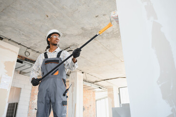 Construction worker painting wall with roller in building under construction