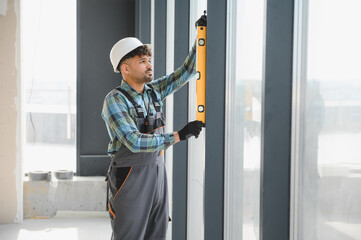 Construction worker checking window frame with spirit level in building under construction