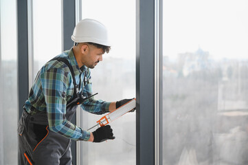 Construction worker sealing window frame in modern building