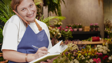 The florist is talking on the phone, smiling, and writing down business notes in a notebook. Small business. Close-Up.
