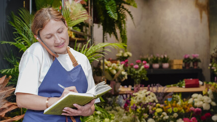 The florist is talking on the phone, smiling, and writing down business notes in a notebook. Small business. Close-Up.