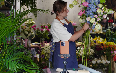 Florist conducts online training on creating bouquets using a phone. Florist records instructional...