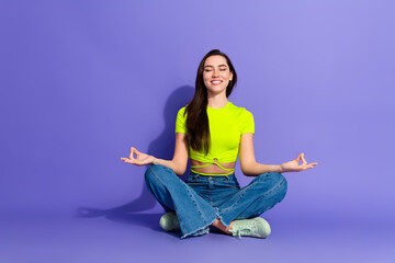Young woman in casual attire meditating in lotus pose on a purple background, promoting relaxation,...