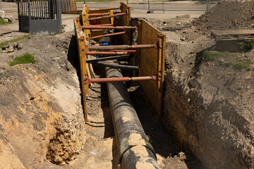 The excavated trench boasts a large pipe and various safety equipment used for construction and...