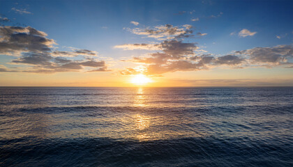 Fototapeta premium a serene scene of the early morning sun rising above the horizon casting a golden glow over the tranquil ocean water with a few scattered clouds