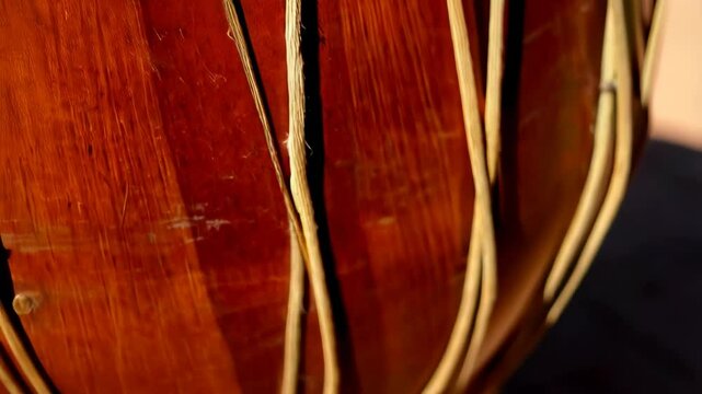 Close-up on aged two-headed drum, featuring tan ropes, sunlight, and shadow against a textured earthen background, capturing an ethnic percussion instrument.