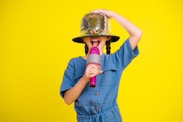 Cheerful girl singing with pink microphone wearing disco hat and blue outfit against vibrant yellow...