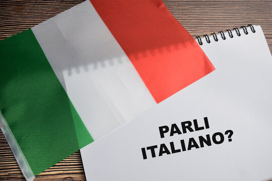 Concept of with question parli italiano write on book and flag of Italy isolated on Wooden Table.