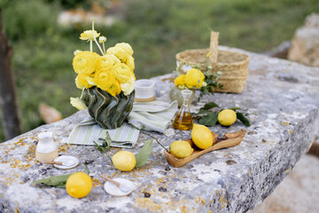 Close-up of a rustic stone table styled with bright yellow ranunculus flowers, fresh lemons with...