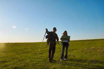 Young Couple Hiking with Trekking Poles in Open Green Field