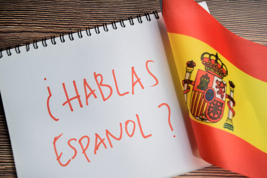 Concept of with question hablas espanol write on book and flag of spain isolated on Wooden Table.
