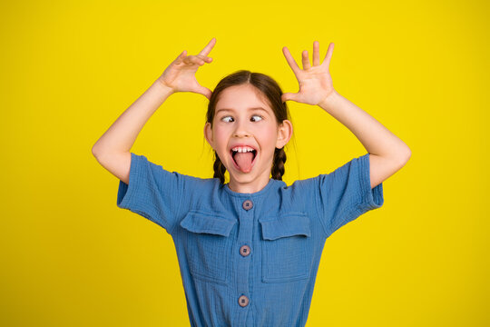 Cheerful young girl making funny faces with a bright yellow background showcasing playful and joyful childhood moments - Powered by Adobe
