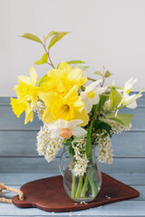 Bouquet of daffodils and small white cherry blossoms in a glass clear pitcher on a blue wooden surface. . Wallpaper, holiday picture
