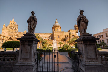 Obraz premium The grand entrance of Palermo Cathedral framed by Moorish arches and lush palm trees, bathed in the golden evening light. A timeless blend of cultures in the heart of Sicily