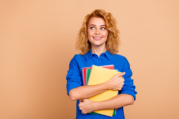 Young woman with curly red hair holding colorful notebooks in a cheerful and modern casual style against a beige background