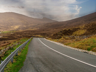 A road with a mountain in the background. The road is empty and the sky is cloudy. There is metal...