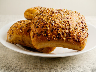 Three crusty rolls with seeds and grain in white bowl on simple light color table cloth. Fine bakery product made from high quality ingredients, Small bread.