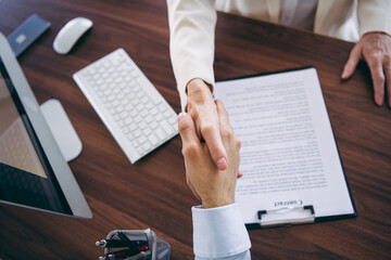 Professional handshake between individuals in a business setting with written document and office...