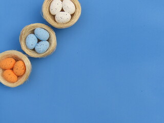 Straw nests with decorated Easter egss on blue background. Easter background. Bird nests crafts. 