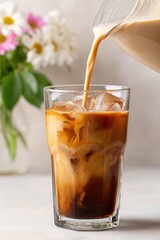 Iced coffee beverage being poured into a clear glass filled with ice, showcasing rich colors and textures, with a soft floral background enhancing the refreshing drink experience