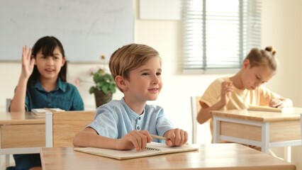 Smart elementary student looking at teacher while attend in classroom. Diverse smart student sitting at classroom while listening teacher explain about classwork or test. Education concept. Pedagogy.