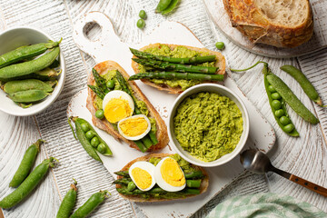 Top view of toast with green pea spread, asparagus and hard boiled egg on a white wooden board. Spring, homemade appetizer, healthy breakfast.