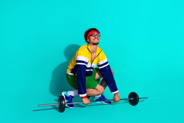 Young male athlete in retro sportswear lifting weights against a vibrant teal background with a...