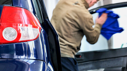 Car wash employee cleaning vehicle window with microfiber cloth