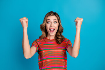 Excited young woman celebrates success with expressive gestures in stylish clothing on a vibrant blue background