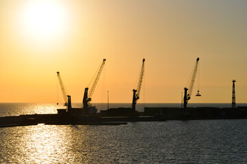 Fototapeta premium Silhouette of container and gantry cranes at abstract port on evening and sun flares background.