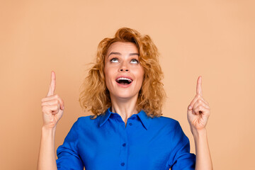Cheerful female in a blue shirt excitedly gesturing upwards against a beige background, showing enthusiasm and positivity
