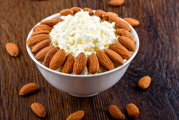 Fresh cottage cheese and almond nuts in a white bowl on a wooden background.