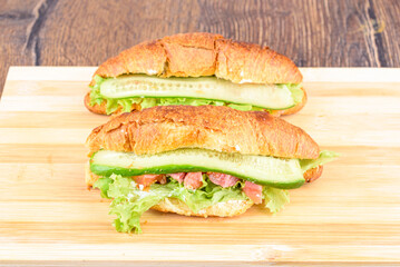 Croissants with lettuce, soft cheese and red fish with cucumber on a cutting board.