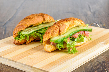 Two croissants with lettuce, soft cheese and red fish with cucumber.