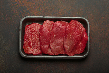 Fresh raw beef meat in a black plastic container on a dark background, ready for cooking juicy steaks. High protein and delicious