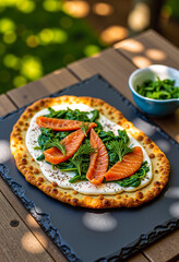 Flexitarian Chickpea and spinach flatbread with smoked salmon, creamy spread, fresh dill, and black pepper on slate board