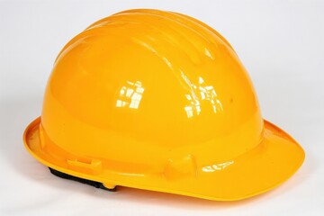 Fototapeta premium A bright yellow hard hat is placed on a plain white surface, designed for safety in construction and industrial environments. The rounded shape and smooth texture highlight its durable design.