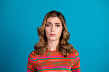 Fototapeta premium Portrait of a thoughtful young woman in a colorful outfit against a blue background, looking expressive with a questioning expression