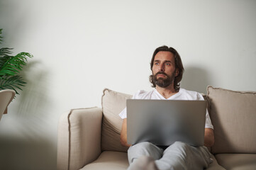 Man Sitting on a Couch Using a Laptop in a Minimalist Living Room