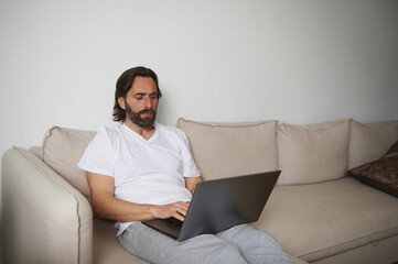 Man Using Laptop While Sitting Comfortably at Home on a Beige Sofa