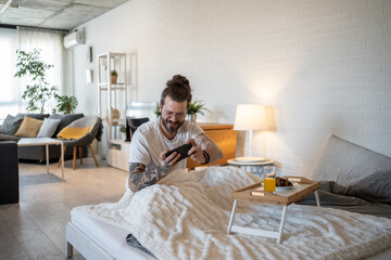 Obraz premium Happy freelancer playing mobile game in bed after waking up