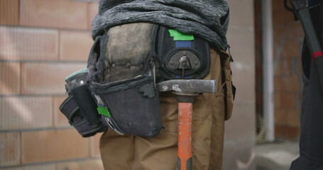 Close-up of construction worker&rsquo;s tool belt with hammer and various equipment, highlighting essential tools for construction and labor tasks in an active construction setting