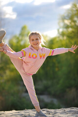 Funny blond girl playing and doing splits outdoor on nature in the summer. Active kid doing yoga exercise. Happy childhood