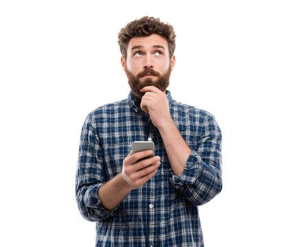 A man with a beard, holding a phone, looks up thoughtfully with hand on his chin.